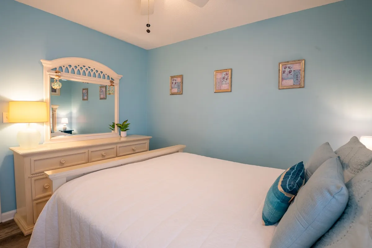 A serene guest bedroom featuring a comfortable bed, a large mirror, a dresser, wall art, and a soft lamp glow. The ambiance is peaceful and inviting, reflecting the comfort and privacy available to all guests.