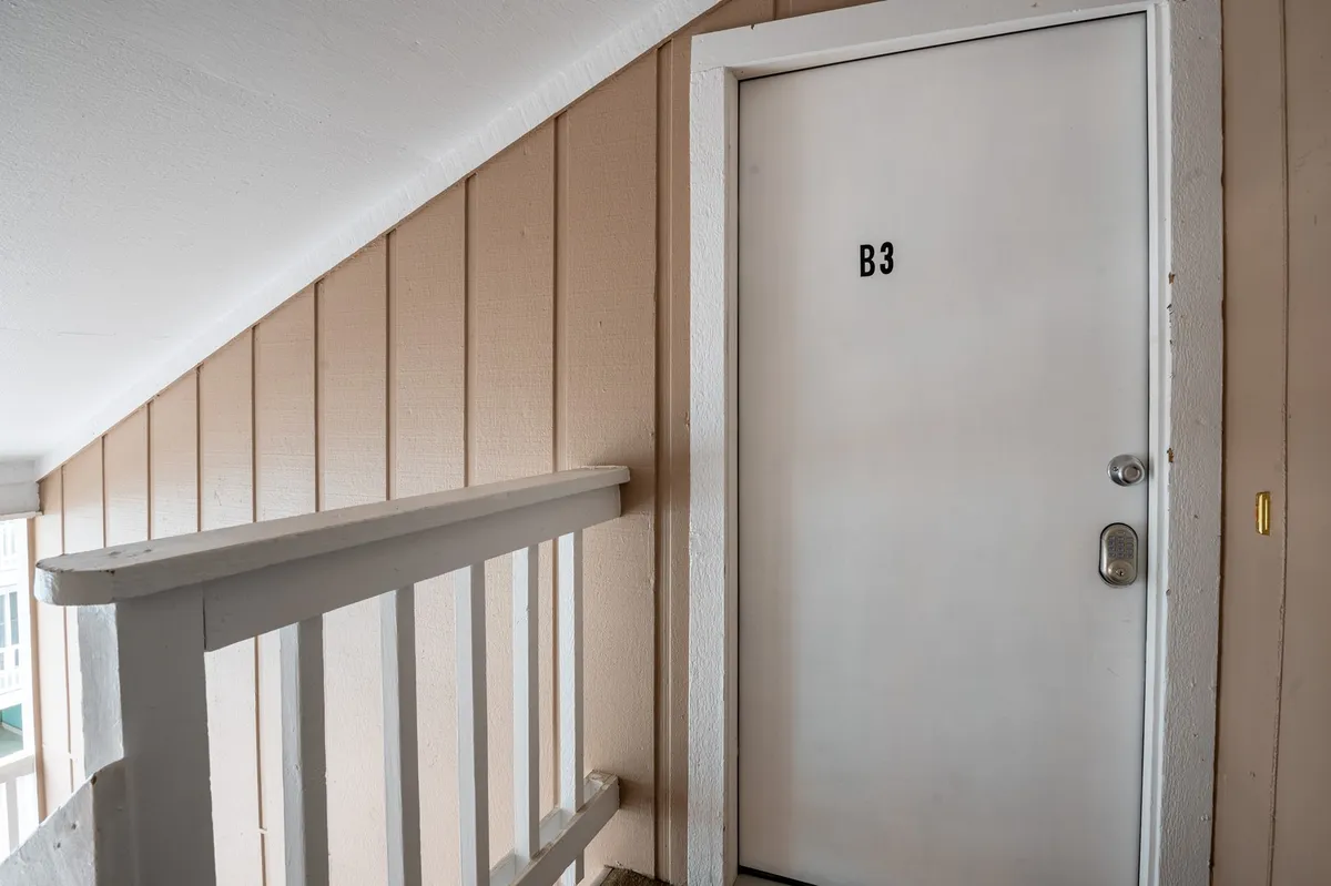 This image shows the exterior entryway to the condo, featuring a door marked 'B3' and a staircase railing. The space is brightly lit and welcomes guests as they arrive or depart, with the stairwell hinting at the elevated position of the property.