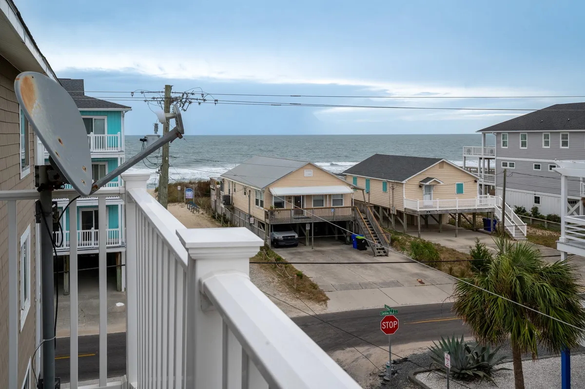 A scenic view of the ocean, beach houses, palm trees, and a stop sign, capturing the tranquil beach neighborhood. The image suggests easy access to the beach and local attractions, fitting the narrative of group activities and exploration.