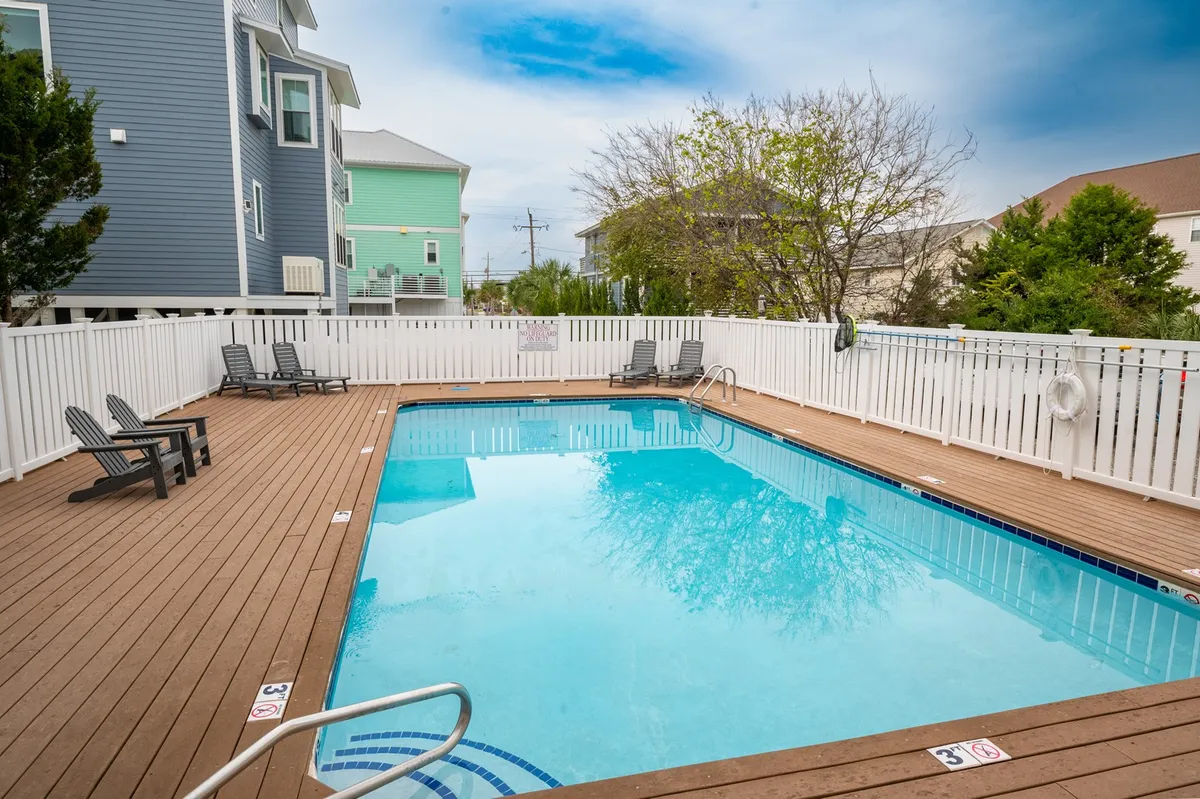 A bright, inviting pool area with sparkling water, deck chairs, and lush greenery creating a relaxed atmosphere. The scene suggests a place for swimming, sunbathing, and family-friendly gatherings.